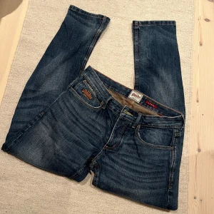 Mörkblå jeans från Superdry - Säljer ett par mörkblå jeans från Superdry med klassisk femficksdesign och snygga slitningar. Jeansen är straight och inte särskilt loose enligt mig. Storlek W30 L32. Skriv om frågor eller förslag på pris.