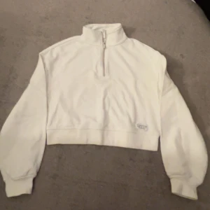 Vit croppad half zip från H&M Divided - Säljer en vit croppad sweatshirt från H&M Divided med half zip och hög krage. Tröjan har långa ärmar och är tillverkad i mjuk bomullsmix. Perfekt för en chill och stilren look.