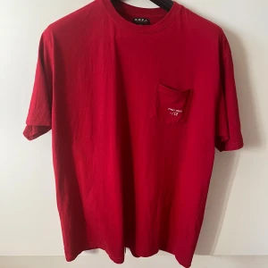 Röd t-shirt från G.O.F.F. strl XXL - Röd t-shirt från G.O.F.F. i storlek XXL. Klassisk modell med rund hals, kort ärm och bröstficka med vit text. Vit detalj på ena ärmen. Tillverkad i 100% bomull. Har tyvärr ett litet hål på tröjans baksida.