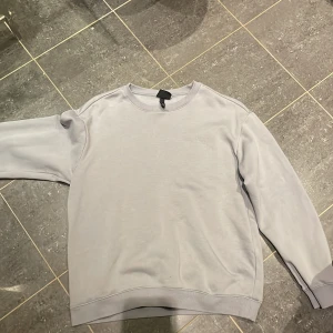 Ljusgrå sweatshirt från H&M - En stilren ljusgrå sweatshirt från H&M i relaxed fit. Tröjan har rund halsringning, ribbade muddar vid ärmslut och nederkant samt är tillverkad i mjuk bomullsblandning. Perfekt för en chill och enkel look.