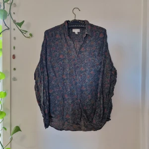 Mjuk, tunn skjorta i abstract blommigt tyg. - Mjuk, tunn skjorta i abstract blommigt tyg. Första bilden är färgerna i dagsljus och andra är i varmt lampljus. (Säljer åt min partner)