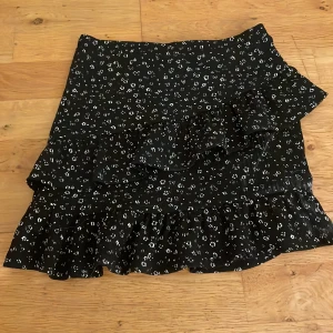 Svart volangkjol med blommigt mönster - Supersöt svart kortkjol med små vita blommor och volangdetaljer. Den är i storlek 146/152 från Kappahl men för mig som är 162 passar den ändå eftersom den nog ska vara lite längre men då blir den istället kortare. Skulle säga att någon som har storlek Xs/S kan ha den. Den är tajtare och har volanger.