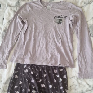 Mörklila pyjamasbyxor med rymdmönster - Mysiga mörklila pyjamasbyxor från Kappahl med coolt rymdmönster av planeter, stjärnor, raketer och hjärtan i vitt och lila. Byxorna är raka i modellen och tillverkade i mjuk bomull, perfekta för chillkvällar hemma.