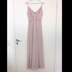 Ljusrosa långklänning med smala axelband - Elegant ljusrosa långklänning som är helt ny, är endast provad. Klänningen har smala axelband och v-ringning. Tunt, flytande material som ger ett mjukt fall. Perfekt för speciella tillfällen.