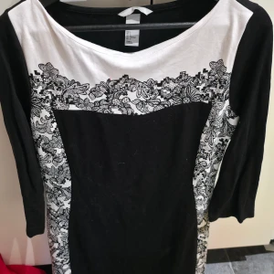Svartvit blommig klänning från H&M - Snygg svartvit klänning från H&M i storlek L med blommigt mönster längs sidorna och upptill. Klänningen är tillverkad i mjuk viskosblandning med polyester och elastan för skön passform. Perfekt för dig som gillar kontraster och detaljer.