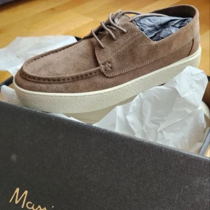 Bruna mocka loafers från Massimo Dutti - Säljer ett par snygga bruna loafers från Massimo Dutti i mjuk mocka. Skorna har vit platt sula, snörning och klassisk seglarsko-look. Perfekta för dig som gillar stilrena och bekväma skor med modern touch.