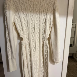 Vit stickad klänning från Adoore - Superfin vit stickad klänning från Adoore med kabelstickat mönster och rund halsringning. Långärmad och figurnära passform som markerar midjan. 