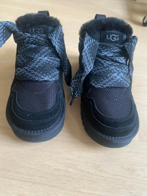 Svarta UGG lowmel - Säljer ett par splitternya svarta UGG lowmel med fluffig päls på insidan och grov yttersula. Skorna har breda, mönstrade snören och detaljer i mocka och syntet. Andra snören medföljer.  Stl 38. Säljer pga att storleken var för liten sår 39 på kartongen (stl.8) men är mer som 37-38.