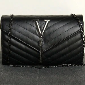 Svart väska - Snygg svart väska med kedja som axelrem. Kedjan går att styra längden på. Väskan har ett innerfack med dragkedja och snyggt mönstrad yta. Stilren och praktisk väska med det lilla extra.