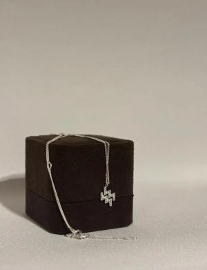 ANI halsband med glittrig berlock - Snyggt halsband från ANI i silverfärg med en glittrig, geometrisk berlock täckt av små stenar. Kedjan är tunn och elegant, perfekt för att ge en extra touch till din stil. Kommer i en lyxig ask med svart insida.