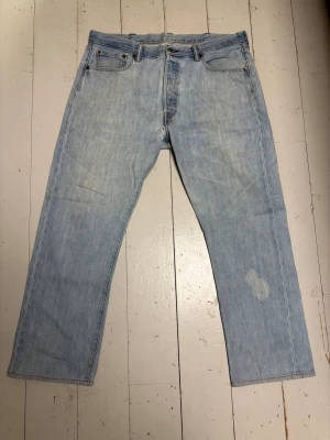 Vintage Levis 501 ljusblå jeans straight fit - Ljusblå Levi's 501 jeans med klassisk rak passform. Jeansen har knappgylf, tydliga Levi's-detaljer och är tillverkade i slitstarkt bomullsjeans. Perfekt för dig som gillar en avslappnad och tidlös look. Köpte dessa second hand. De har en blekningsfläck på ena benet men tycker den är rätt najs när de är på, gör de unika på de sättet. Skulle säga att de sitter 33/31. Lite stora i midjan men med bälte är det inga problem. Jag brukar ha 32/32. 