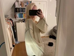 Vit stickad tröja från Gina Tricot med coola detaljer  - Säljer en krämvit stickad tröja från Gina Tricot med breda ärmar och svarta dekorativa sömmar längs axlar och ärmar. Tröjan har en rund halsringning och en loose fit som ger en chill vibe. Perfekt för lager-på-lager under hösten och vintern.