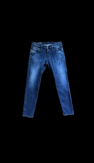 Replay jeans - Säljer ett par snygga Replay Anbass jeans i klassisk blå färg. Modellen har raka ben med lätt tapered passform och coola detaljer på bakfickorna. Jeansen är tillverkade i slitstarkt denim och har en normal midja. Perfekt för dig som gillar stilrena jeans med modern touch.