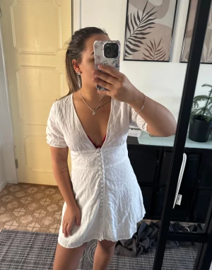 Studentklänning från Boohoo - Supersöt vit kort klänning från Boohoo med broderade blommor, v-ringning och knappar framtill🥰 Klänningen har korta puffärmar och markerad midja som ger en fin siluett. Storlek 36 men passar 34 med. Perfekt för studenten. Använd gärna KÖP NU❣️