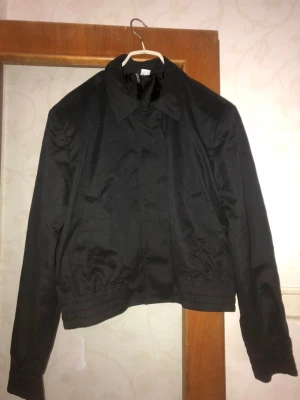 Svart bomberjacka från H&M Divided - Svart bomberjacka från H&M Divided i storlek M. Jackan har klassisk krage, elastisk midja och är helsvart utan mönster. Tillverkad i polyester med slät yta och hel dragkedja framtill. Perfekt för dig som gillar en clean och enkel stil.
