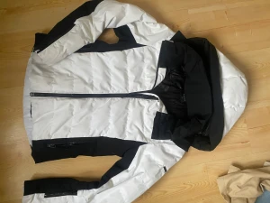 Vit och svart pufferjacka med huva - Jättefin varm skidjacka som passar perfekt till vintern, använts en del men det syns inte. Har även en ficka vid armen där man kan lägga liftkortet. Original pris: 2000