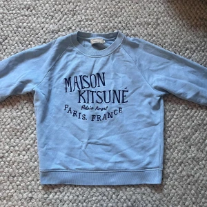 Ljusblå sweatshirt Maison Kitsuné🙌 - Snygg ljusblå sweatshirt från Maison Kitsuné med tryck i mörkblått framtill. Tröjan har rund hals, långa ärmar och ribbade muddar vid hals, ärmslut och nederkant. Perfekt för dig som gillar fransk streetstyle och vill ha en chill vibe.🙌