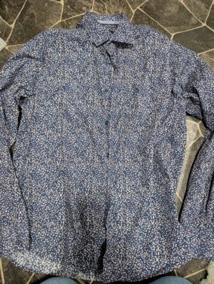 Blommig blå skjorta från F.S. Shirtmaker stl L - Snygg blå skjorta från F.S. Finest Shirtmaker med små blommor i vitt, rött och blått. Skjortan har klassisk krage, knäppning framtill och är tillverkad i 100% bomull. Regular fit och långärmad – perfekt för dig som gillar mönster och vill sticka ut lite extra. Fint skick