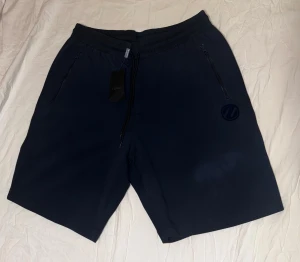 Marinblå shorts från Zegna - Snygga marinblå shorts från Zegna med elastisk midja och snörning. De har två praktiska fickor med dragkedja och en diskret logga på ena benet. Perfekta för chill dagar eller träning, tillverkade i mjukt material som känns skönt mot huden.