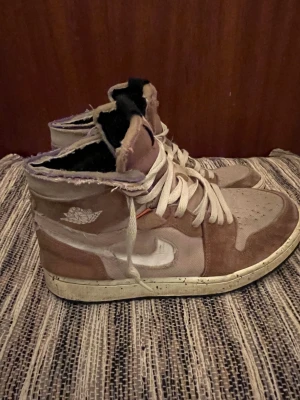 Nike Jordan 1 Zoom Air Highs beige - Nike Jordan 1 Zoom Air sneakers i high-top modell med beige och bruna toner. Storlek: 42. Skorna har snörning, rund tå och platt sula. Materialmix av mocka och textil med slitna, råa kanter för en edgy vibe. Swoosh-logga i vitt och klassisk Air Jordan-vinge på sidan.