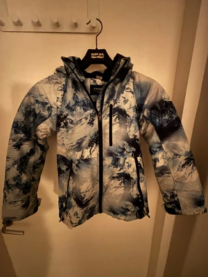 Blåvit pufferjacka från Everest - Säljer en blåvit pufferjacka från Everest med coolt bergsmönster. Jackan har huva, dragkedja framtill och praktiska fickor. Perfekt för kalla dagar när du vill sticka ut med en häftig look. Helt oanvänd. Storlek 134. Hör av dig via e-mejl eller mobilnummer då jag inte kan ta emot Swish på detta nummer. E-mejl emli.com@icloud.com mobil-0728875624