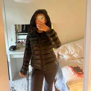 Svart moncler jacka - Svart moncler pufferjacka med glansig yta och huva. Jackan har quiltad design, dragkedja framtill och långa ärmar. Snygg och varm för kalla dagar, med en klassisk look som funkar till jeans eller mjukis. Perfekt för dig som gillar streetstyle och vill ha en jacka som sticker ut. ( slitningar under armhålerba och vid armen det ser ni på bilderna ). Köpt för 6000! Storlek ”14år” passar mig som bär S