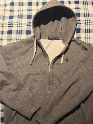 Grå hoodie från Polo Ralph Lauren - Snygg grå hoodie från Polo Ralph Lauren med huva och snörning. Storlek M men sitter mer åt S hållet. Tröjan har dragkedja framtill och klassisk Polo-logga broderad på bröstet. Mjuk insida och ribbade muddar vid ärmslut och nederkant. Perfekt för chill dagar och streetwear. Pris kan diskuteras vid snabb affär.
