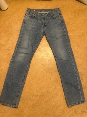 Levi's 514 blå jeans W31 L34 - Säljer ett par klassiska Levi's 514 jeans i ljusblå tvätt. Modellen har rak passform och fem fickor, med snygga detaljer som den bruna läderpatchen bak. Perfekt för dig som gillar tidlös stil och vill ha jeans med skön känsla.köpt för 900kr säljer 500kr(pris kan diskuteras)