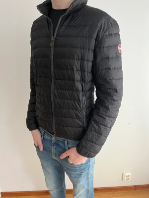 Colmar puffer jacket - Säljer en svart pufferjacka från Colmar med diskret logga på ärmen. Jackan har quiltad design, hög krage och dragkedja framtill. Tillverkad i lätt syntetmaterial och passar perfekt för kyliga dagar. Snygg och stilren modell som funkar till det mesta.
