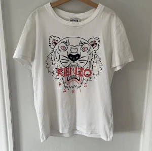 Vit Kenzo t-shirt med tigertryck - Säljer denna snygga vita t-shirt från Kenzo med ett ikoniskt rosa tigertryck. T-shirten är i nytt skick och köpt på Therlunds i Mall of scandinavia.