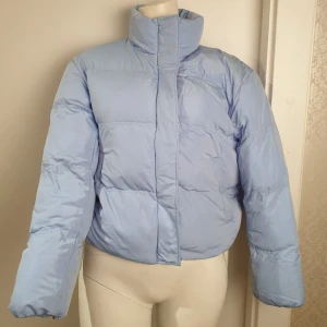 Ljusblå pufferjacka - Säljer en ljusblå pufferjacka med dragkedja och knappar. Jackan har en hög krage och långa ärmar, perfekt för kyliga dagar. Den är stilren och enkel att matcha med olika outfits. ❗Har fläckar och behöver tvättas, därav priset.