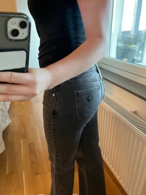 Svarta boot jeans från Abrand - Säljer ett par svarta jeans från Abrand med snygg tvättad look och raka, breda ben. Modellen är högmidjad och har klassiska fem fickor samt logga på bakfickan. Jeansen är tillverkade i jeansmaterial och har dragkedja och knapp framtill.