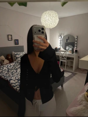 Svart omlottopp med knyt framtill - Säljer en svart långärmad omlottopp med djup v-ringning och knyt framtill. Toppen är croppad och har en slim passform som framhäver midjan. Perfekt för dig som gillar trendiga och stilrena plagg.