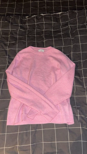 Rosa stickad tröja  - Mysig rosa stickad tröja från vero Moda med rund hals och långa ärmar. Tröjan har ribbade muddar vid ärmslut och nederkant, perfekt för att hålla värmen under kyliga dagar. Enkel och stilren design som är lätt att matcha med dina favoritjeans. Passar även storlek S