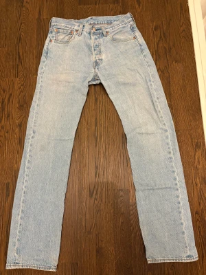 Levi's 501 ljusblå jeans straight fit - Ljusblå Levi's 501 jeans med klassisk straight fit och fem fickor. Jeansen har knappgylf och den ikoniska läderpatchen bak. Tillverkade i slitstarkt bomullsjeansmaterial. Nypris 1500 Säljs nu för 399 i bra skick, förutom lite slitning nertill. W 29 L 32