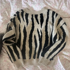 Beige och svart zebramönstrad stickad tröja - Säljer en beige stickad tröja med svart zebramönster. Tröjan har rund halsringning, ribbade muddar och långa ärmar. Perfekt för dig som vill sticka ut med ett djurmönster och gillar en mysig, oversized vibe.