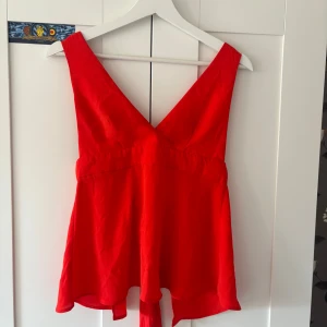 Röd omlottopp från Gina Tricot - Snygg röd omlottopp från Gina Tricot i storlek 34. Toppen har djup v-ringning både fram och bak samt breda axelband. Knytband i ryggen ger en extra detalj och toppen har en lätt utsvängd passform. Perfekt för dig som vill sticka ut med färg. Jättefin på fest, och skulle säga att den inte är så skriktöd som på bilderna. En väldigt liten fläck på ena bröstet med det smälter in i sömarna!