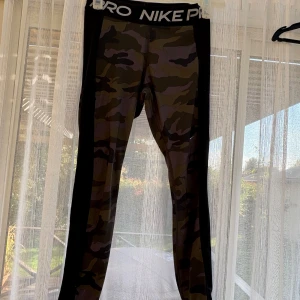 Nike Pro camo tights i medium - Nike Pro tights med camouflagemönster och bred svart resår i midjan med logga. Tight passform och stretchigt material som passar perfekt till träning. Snygga detaljer med svarta paneler längs sidorna.