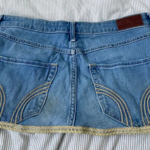 Jeanskjol med guldiga detaljer Hollister - Snygg ljusblå jeanskjol från Hollister med guldiga broderade detaljer längs nederkanten och bakfickorna. Kjolen har mindre fläckor på framsidan och en större på baksidan som man kan se på bild 4 och 5. Kontakta gärna vid frågor💕