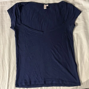 Romance Shape top från Nelly - Supersnygg mörkblå topp från Nelly med v-ringning och spetskant längs urringningen. Modellen är figurnära med korta ärmar och croppad passform. Perfekt att styla med jeans eller kjol för en trendig look.