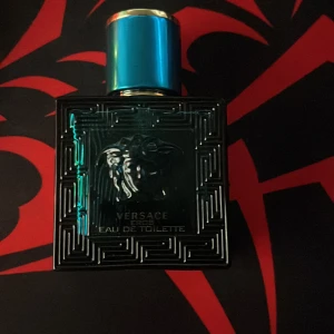 Versace Eros Eau de Toilette med ungefär 25ml kvar - Versace Eros Eau de Toilette med ikonisk Medusa-detalj på flaskan. Flaskan är fyrkantig i mörk turkos glas med geometriskt mönster och har ett metalliskt blått lock. En parfym med lyxig och modern design, perfekt för dig som gillar statement-detaljer.