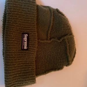 Olivgrön Supreme mössa med patch - Säljer en grön Supreme mössa i stickad modell. Klassisk design med uppvikt kant och Supreme-loggan framtill. Bekväm och varm, perfekt för höst och vinter. Mössan är aldrig använd då jag använde den som en samling pryl eftersom att jag var besatt av supreme förut. Mössan är köpt i USA (äkta) på en supreme butik 2020 (limited edition)