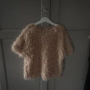 Beige fluffig tröja från Zara - Supermjuk och fluffig beige tröja från Zara med korta ärmar. Tröjan har en cool pälsliknande look och är perfekt för dig som vill sticka ut med en mysig och trendig stil. Passar lika bra till jeans som till kjol.