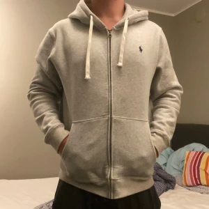 Polo Ralph Lauren Hoodie Storlek L - Snygg ljusgrå hoodie från Polo Ralph Lauren med dragkedja, huva med vita snören och klassisk broderad logga på bröstet. Tillverkad i mjuk bomullsmix och har känguruficka framtill. Perfekt för chill dagar eller när du vill ha en clean streetstyle. Pris kan diskuteras! 