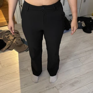 Svarta kostymbyxor från Lindex - Snygga svarta kostymbyxor från Lindex med klassisk rak passform och highwaist. Byxorna har knapp och dragkedja framtill, bälteshällor och fickor fram dom där bak e bara för prydnad. Perfekta för en clean och stilren look.