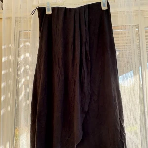 Svart omlottkjol från Pieces - Svart långkjol från Pieces i omlottmodell. Kjolen har en enkel och stilren design med lätt rynk vid midjan och är tillverkad i ett mjukt tyg som känns skönt mot huden. Perfekt för dig som gillar en avslappnad men ändå snygg look.