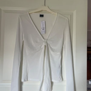 Vit långärmad topp Gina Tricot - Säljer en vit långärmad topp från Gina Tricot med snygg v-ringning och knyt framtill. Enkel och stilren design som passar till allt✨ Lägg ett bud