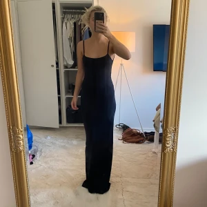 Svart långklänning med smala axelband - Säljer en svart långklänning med smala axelband och öppen rygg. Klänningen har en tight passform och ärmlös design som ger en stilren och elegant look. Perfekt för dig som gillar minimalistisk stil och vill sticka ut med en klassisk siluett.