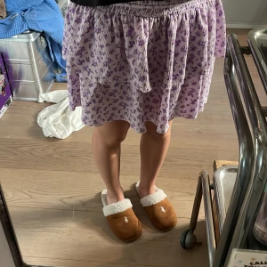 Ljuslila blommig volangkjol - Supersöt kort kjol i ljuslila med små blommor och volangdetaljer. Kjolen har stretch i midjan för en bekväm passform och är perfekt för varma dagar. Tunt och luftigt material som känns lätt att bära. Lappen är avklippt.