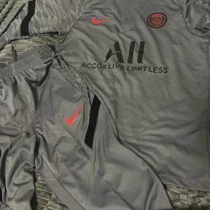 Grå PSG fotbollströja från Nike M - Säljer en grå Paris Saint-Germain fotbollströja från Nike i Dri-FIT material. Tröjan har korta ärmar med subtila zebramönster och svarta detaljer, samt röd Nike-logga och PSG-märke på bröstet. Perfekt för träning eller match!